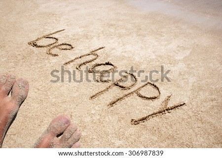 Concept or conceptual Be happy text handwritten in sand on a beach with feet in an exotic island for tropical, summer, sea, ocean, calendar, travel, holiday, sunny, tourism, resort, time or relaxet