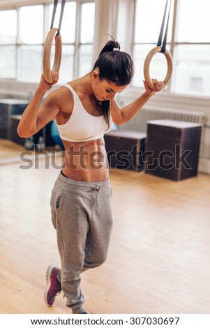 Fit young woman exercising with gymnastic rings. Muscular woman at gym looking down, preparing from training session.