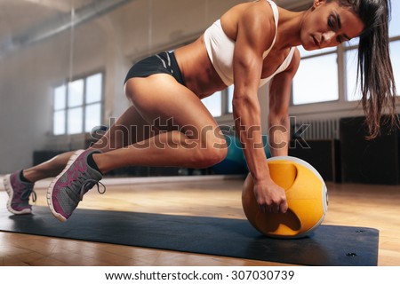 Muscular woman doing intense core workout in gym. Strong female doing core exercise on fitness mat with medicine ball in health club. Royalty-Free Stock Photo #307030739