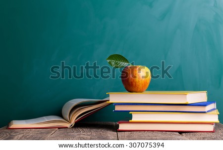 Still life with school books and apple against blackboard with "back to school" on background