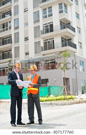 Contractor and investor standing in front of the building and discussing construction plan