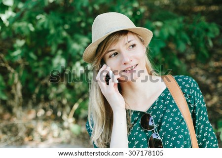 Pretty young girl in a straw hat calling on a mobile phone outdoors among trees
