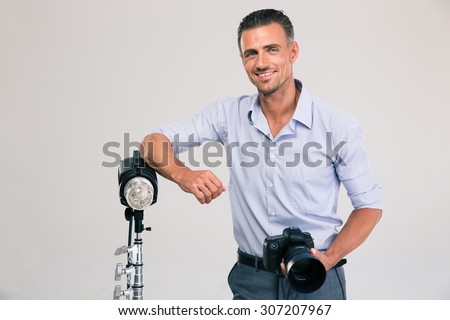 Portrait of a cheerful young photographer standing with camera isolated on a white background and looking at camera