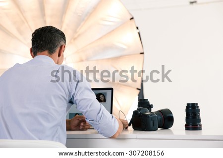 Back view portrait of photographer using laptop at his workplace