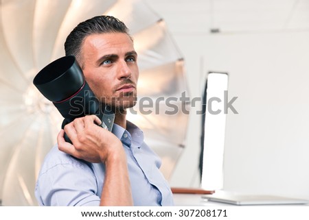 Portrait of a thoughtful photographer holding camera and looking at camera in studio