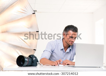 Portrait of a happy photographer using laptop at his workplace