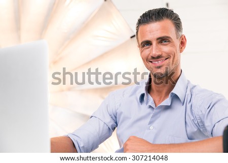 Happy confident man using laptop and looking at camera in studio