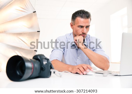 Portrait of a handsome photographer using laptop at his workplace