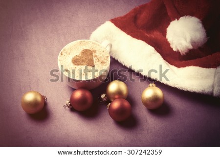 Cup of coffee with heart shape near Santas hat and christmas bubbles. Photo in old color image style.