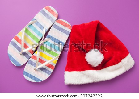 Santas hat and flip flops on violet background.