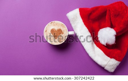 Cup of coffee and christmas hat on violet background.