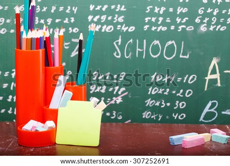 Colorful pencils of red yellow orange violet purple pink green and blue in stationary cup and stick on brown school desk on written with white chalk blackboard background copyspace, horizontal picture