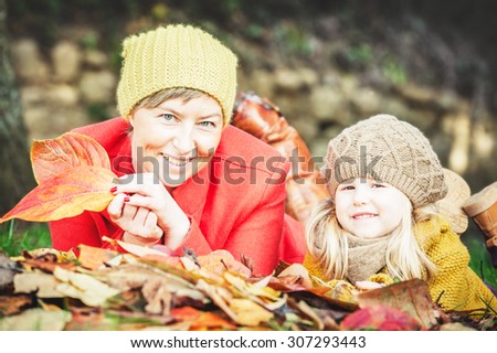 Beautiful mother and daughter playing in the park in autumn colored leaves