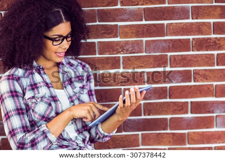 Attractive hipster leaning on wall and using tablet against red brick background