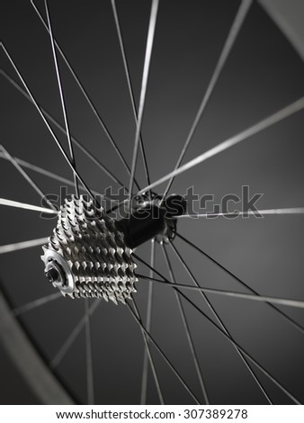 Shot of bicycle wheel showing gears or cogs with a shallow depth of field showing spokes and rim. The shot has bee taken in the studio and has a monochrome feel due to metal and carbon in the pic. 