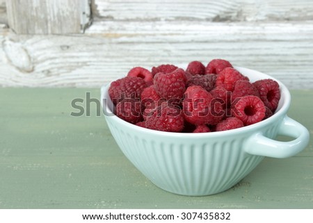 Tureen with red raspberries with green and white wooden background