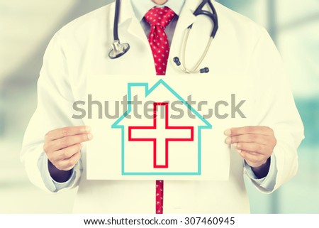 Closeup doctor hands holding white paper house with red cross sign isolated on hospital clinic office background. Retro instagram style filter image