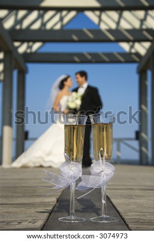 Pair of flute glasses of champagne with Caucasian bride and groom blurred in background.