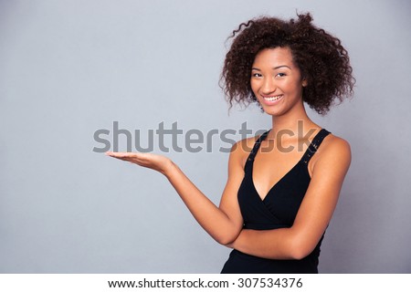 Portrait of a smiling african woman holding copyspace on the palm over gray background and looking at camera