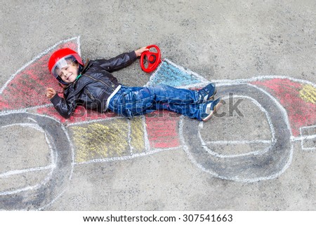 Happy little child of four years having fun with race car picture drawing with colorful chalks. Creative leisure for children outdoors in summer. Kid boy dreaming to be a racer