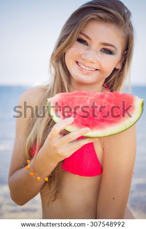 Beauty smiling teenager girl is wearing pink bikini and eating watermelon near sea