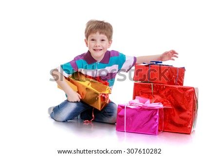 Funny little brown-eyed boy sitting on the floor. Next to the boy lay the box with gifts-Isolated on white background