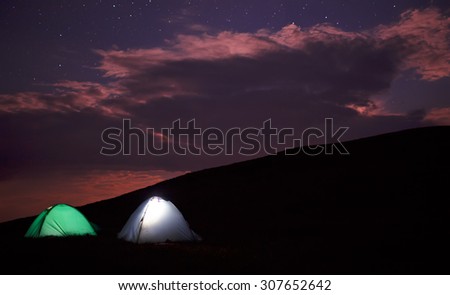 Lighted camping tents in mountains at night.