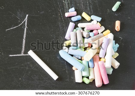 One piece of chalk against the pile of crayons of different colors on a black background blackboard opposition, number one. one in a thousand