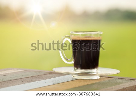 Black coffee with green meadow in background and the sunrise.