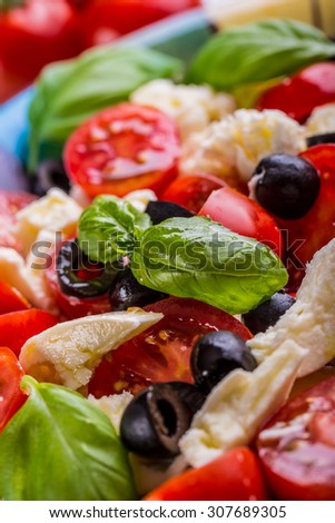 Caprese Italian or Mediterranean salad Tomato mozzarella basil leaves black olives and olive oil.