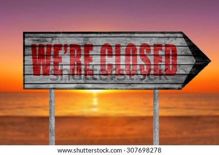 Red We're Closed wooden sign with on a beach background