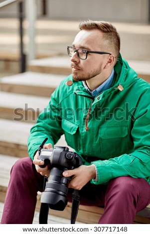 people, photography, technology, leisure and lifestyle - young hipster man holding digital camera with big lens and sitting on stairs in city