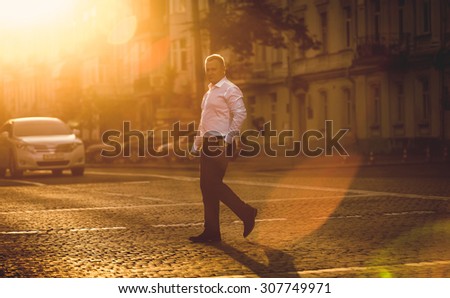 Toned photo of elegant businessman crossing street at sunny day