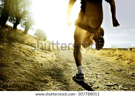 close up silhouette legs and feet of extreme cross country man running and training on rural track jogging at sunset with harsh sunlight and lens flare in countryside sport and healthy lifestyle Royalty-Free Stock Photo #307788011