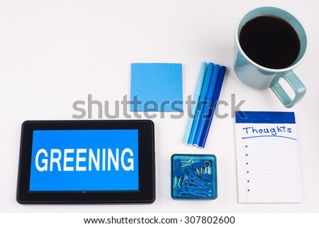Business Term / Business Phrase on Tablet PC - Blues, cup of coffee, Pens, paper clips Calculator with a blue note pad on White - White Word(s) on blue - Greening