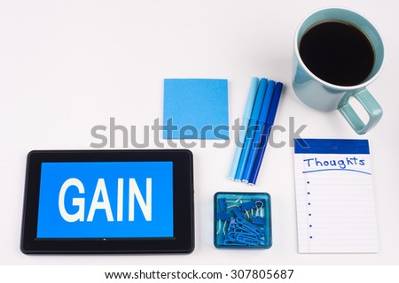 Business Term / Business Phrase on Tablet PC - Blues, cup of coffee, Pens, paper clips Calculator with a blue note pad on White - White Word(s) on blue - Gain