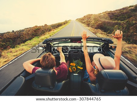 Happy Young Carefree Couple Driving Along Country Road in Convertible at Sunset Royalty-Free Stock Photo #307844765