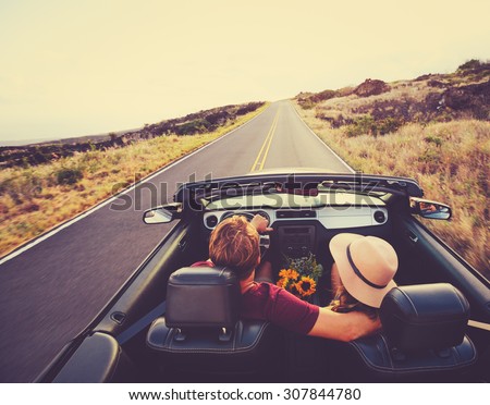 Happy Young Couple Driving Along Country Road in Convertible at Sunset Royalty-Free Stock Photo #307844780