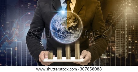 Businessman holding the tablet with earth and stack of golden coins on Trading graph on the cityscape at night and world map background,Elements of this image furnished by NASA
