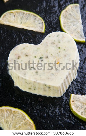 Homemade heart shaped ice cream with basil and lime slices on black stone background