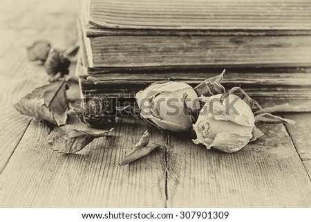 selective focus image of dry rose, antique necklace and old vintage books on wooden table. black and white old style photo
