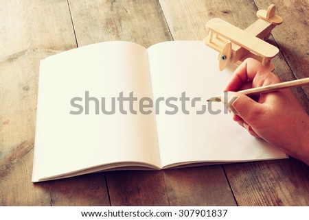 open blank notebook and woman hands next to toy aeroplane on wooden table. retro style filtered image
