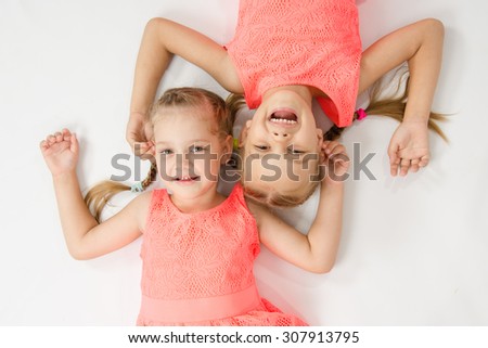 Two girls sisters in the same clothes lie on a white surface next to a head-to-head look at the picture and smiling