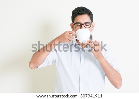 Portrait of handsome casual business Indian guy relax and drinking a cup hot coffee, standing on plain background with shadow, copy space at side.