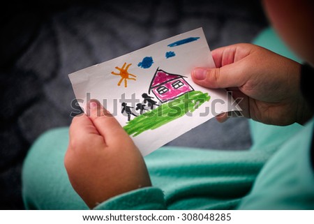 Child holds a drawn house with family. Close up. Vignette.