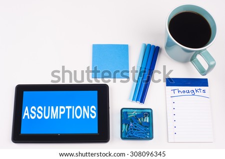 Business Term / Business Phrase on Tablet PC - Blue Colors, Coffee, Pens, Paper Clips and note pads on White - White Word(s) on blue - Assumptions