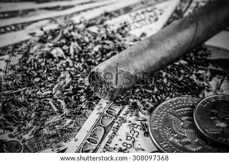 Cuban cigar with coins and tobacco leaves lie scattered on the dollar bills on a wooden table. Close up view, image vignetting in hard black and white tones