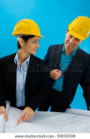 Young architects wearing hardhat looking at blueprint, isolated on blue.