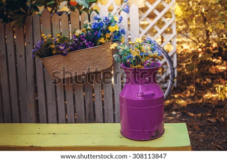 Background: toned photo with a pot of flowers on a bench near the wooden fence in the village in summer