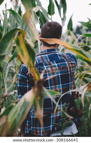 Young hipster man with vintage camera in a corn filed. Vintage retro style effect, soft focus, low light, grain texture visible on maximum size. Horizontal